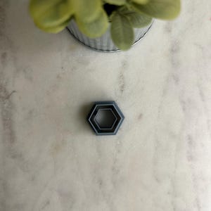 May include: A set of three gray hexagonal cookie cutters, nested inside each other.