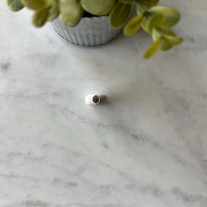 May include: A small white ceramic vase with a rounded opening. The vase is sitting on a white marble surface.
