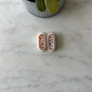 May include: Two light pink oval-shaped cookie cutters with a floral design. The cookie cutters are on a white marble surface.