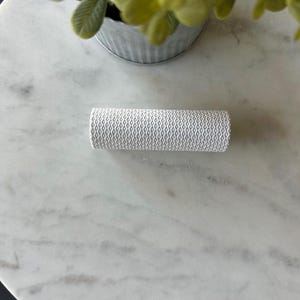 May include: A white textured cylinder on a white marble surface.