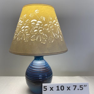May include: A blue and brown ceramic table lamp with a clip-top lampshade. The lampshade is tan and features a floral design. The lamp base is 5 inches wide, 10 inches tall, and 7.5 inches deep. The text "Clip top" is visible.