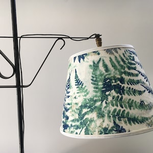 May include: A vintage-style floor lamp with a black metal frame and a lampshade featuring a fern leaf pattern in shades of green and blue on a cream background. The lampshade has a white trim.
