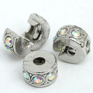 May include: Three silver-toned jewelry clasps with iridescent, round gemstones. One clasp is open, revealing the interior mechanism. The other two clasps are closed, showcasing the decorative gemstones. These clasps are designed for jewelry making.