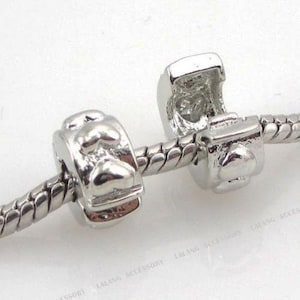 May include: Two silver charm beads with a heart design. The beads are designed to fit on a charm bracelet.