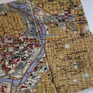 May include: A vintage map of Philadelphia, Pennsylvania, divided into four sections. The map is printed on a beige background with brown, black, and red text and lines. The map shows the Schuylkill River, streets, and landmarks.