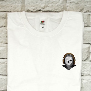 May include: White t-shirt with a small, embroidered image of a skull wearing headphones. The skull is gray and the headphones are brown.