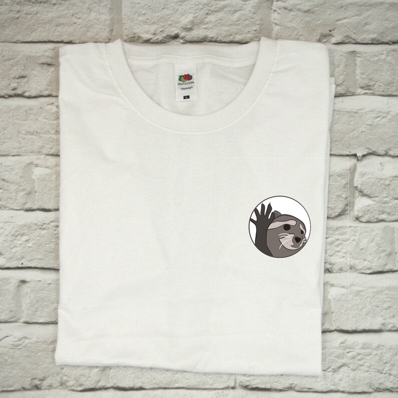 May include: White t-shirt with a small, round, black and white graphic of an otter waving. The otter is looking to the right and has a surprised expression.
