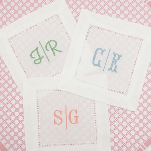 May include: Three white linen napkins with embroidered initials. The initials are "J/R", "C/E", and "S/G".