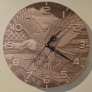 May include: Wooden wall clock with a detailed carving of an American bald eagle with outstretched wings, set against a backdrop of the American flag and a mountain landscape. The clock hands are black, and the numbers are carved into the wood.