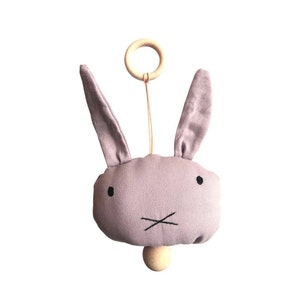 May include: A lavender fabric bunny rattle with a wooden ring and a wooden bead at the bottom.