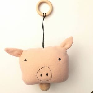 May include: A pink felt pig with black eyes and a snout hanging from a wooden ring. The pig is attached to a wooden dowel.
