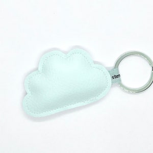 Könnte beinhalten: Ein hellblaues, wolkenförmiges Schlüsselanhänger mit einem silbernen Schlüsselring. Der Schlüsselanhänger besteht aus einem weichen Material und hat eine genähte Kontur. Das Wort "sten" ist auf einem hellblauen Band aufgedruckt.