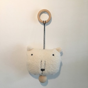 May include: A white plush bear head with black eyes and a black nose hangs from a wooden ring. The bear is attached to a wooden ball that swings.