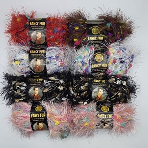 May include: A collection of Lion Brand Fancy Fur yarn skeins in various colors, including red, black, white, and pink. Each skein has a fuzzy texture and is labeled with "Fancy Fur". The yarn is designed for knitting and crafting projects.