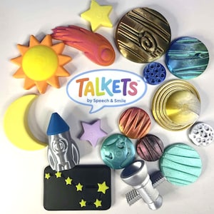 May include: A collection of space-themed plastic tokens and figures including a yellow sun, a crescent moon, a comet, a rocket, a satellite, and various textured planets. A central white speech bubble logo reads TALKETS by Speech & Smile.
