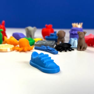 May include: A collection of small, colorful figurines, including a blue sneaker, an octopus, a dog, and a red apple. The figurines are arranged on a white surface against a blue background.