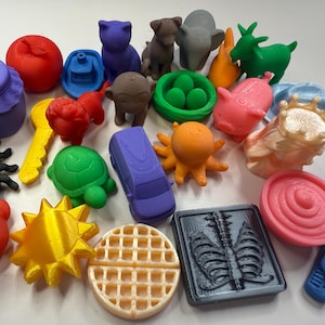 May include: A collection of colorful 3D-printed figurines, including a purple jar, a red apple, a blue boat, a purple cat, a brown dog, a gray elephant, a green goat, and an orange octopus. Other items include a turtle, a car, and a waffle.