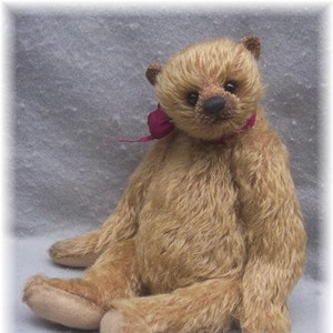 May include: A light brown teddy bear with a red ribbon around its neck. The bear is sitting on a light gray surface.
