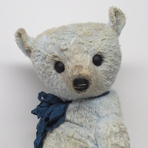 Puede incluir: Un oso de peluche vintage de color azul claro con una pajarita de tela azul. El oso tiene un aspecto desgastado y descolorido y ojos negros de botón.