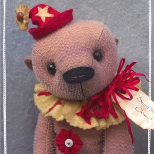 Peut inclure: Un ours en peluche fait main habillé en clown. L'ours porte un chapeau rouge et jaune avec une étoile sur le dessus, un col en dentelle jaune et un nœud rouge. L'ours a un nez noir et des yeux bruns. L'ours tient une pancarte qui dit "Send in the Clowns".