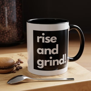 May include: White ceramic mug with a black rim and handle. The mug has a black square with the text "rise and grind!" in white letters.