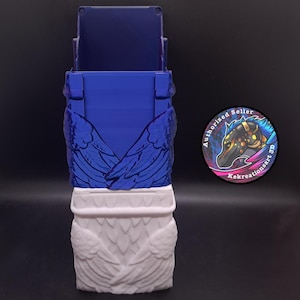 May include: A 3D-printed card holder in blue and white, featuring wing designs. The top section is blue, while the bottom is white. The holder has a rectangular shape with a slot at the top. A circular logo with a horse is visible.