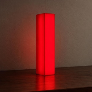 Pode incluir: Uma lâmpada vertical alta e retangular que emite um brilho vermelho vibrante. A estrutura apresenta bordas limpas e nítidas, com uma superfície lisa e uniforme que ilumina a área ao redor com uma luz vermelha intensa e constante.