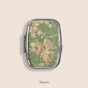 Może przedstawiać: Prostokątne, srebrne pudełko na pigułki z kwiatowym wzorem. Pudełko ma pokrywę na zawiasach i zielone tło z brzoskwiniowymi i żółtymi kwiatami piwonii. Tekst "Misski. Tokyo" znajduje się na dole.