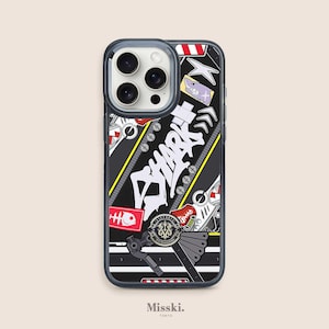 Può includere: Una custodia per telefono nera con una grafica di squalo bianca e rossa, un design a cerniera e altre grafiche colorate. La custodia ha un retro trasparente per mostrare il telefono.