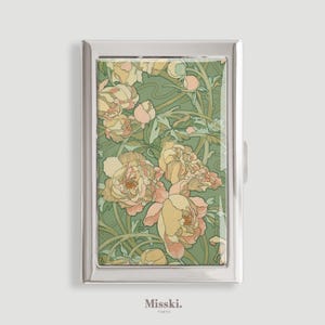 Può includere: Un astuccio rettangolare in metallo argentato con un design floreale. L'astuccio presenta uno sfondo verde con un motivo di peonie e foglie gialle e rosa. Il marchio "Misski. Tokyo" è stampato in basso.