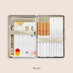 May include: Open silver cigarette case with a selection of cigarettes, a credit card, and a ten-dollar bill. The case is rectangular and has a hinged lid. The cigarettes are white with a brown filter. The credit card has a Mastercard logo.