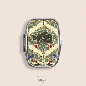May include: A rectangular, silver-framed pill box with a decorative design. The lid features a sleeping black cat surrounded by green leaves, red berries, and blue birds. The text "Misski. Tokyo" is at the bottom.