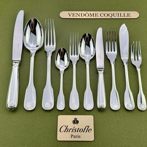 Può includere: Un set di nove posate argentate della collezione Christofle Vendôme Coquille, caratterizzate da un motivo a conchiglia alla base di ogni manico. Il set include coltelli, forchette e cucchiai, con il testo VENDÔME COQUILLE e Christofle Paris.