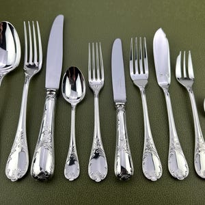 Peut inclure: Ensemble de couverts en argent poli, comprenant des cuillères, des fourchettes et des couteaux, disposés sur une surface verte. L'argenterie présente des détails ornementaux d'inspiration florale sur les manches. L'ensemble comprend des cuillères, des fourchettes et des couteaux de différentes tailles.
