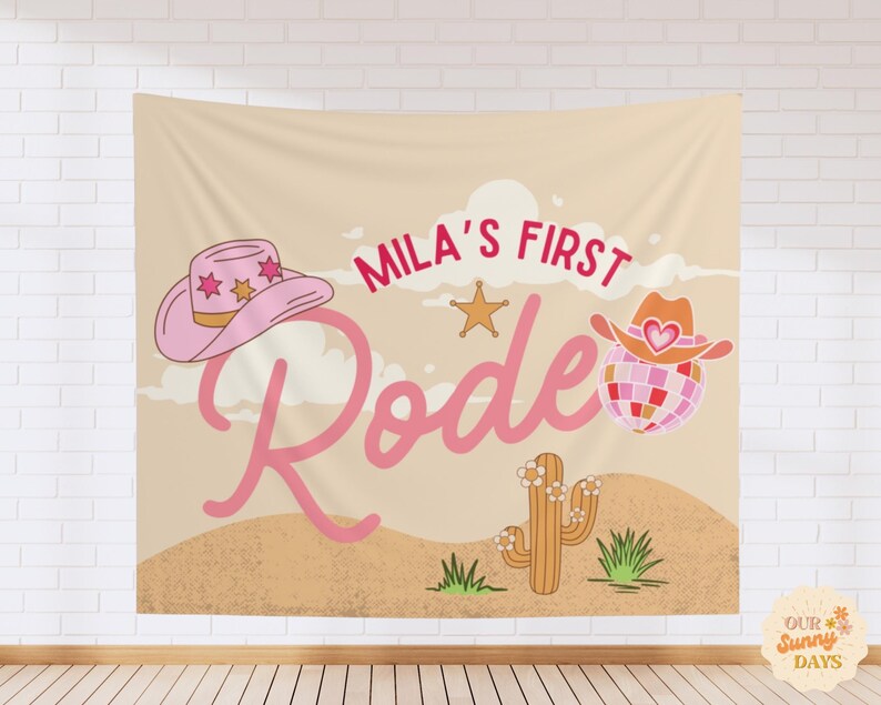 Puede incluir: Un tapiz de pared rectangular de tela con un paisaje des&eacute;rtico beige, un cactus y el texto Mila's First Rodeo en letra cursiva rosa. El dise&ntilde;o incluye un sombrero de vaquero rosa con estrellas, una estrella dorada y una bola de discoteca.