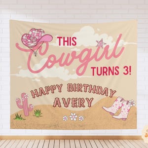 Puede incluir: Un tel&oacute;n de fondo de tela rectangular con un paisaje des&eacute;rtico, un sombrero de vaquero a cuadros rosa, un cactus rosa y botas de vaquero rosas. El texto dice THIS Cowgirl TURNS 3! HAPPY BIRTHDAY AVERY en letras rosas y marrones sobre fondo beige.