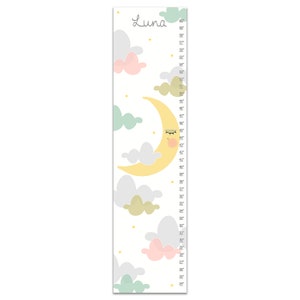 May include: A white growth chart with a yellow crescent moon with a pink face and closed eyes. The moon is surrounded by clouds in shades of pink, green, and gray. The chart has a scale in inches from 24 to 60 inches. The word "Luna" is printed at the top of the chart.