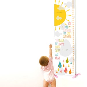 May include: A white growth chart with a yellow sun, gray clouds, and colorful raindrops. The chart has the name "HANNAH" at the top and the text "YOU ARE MY SUNSHINE MY ONLY SUNSHINE YOU MAKE ME HAPPY WHEN SKIES ARE GRAY".
