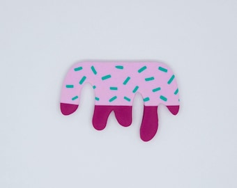 Puede incluir: Una forma de fieltro rosa y morado que se asemeja a un cono de helado que gotea con chispas verdes.