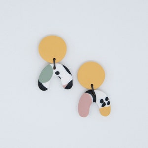 Può includere: Un paio di orecchini astratti colorati con un design giallo, rosa, verde, nero e bianco. Gli orecchini sono realizzati in pasta polimerica e hanno uno stile unico e moderno.