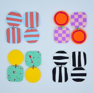 Peut inclure: Quatre paires de boucles d'oreilles en argile polymère colorées. Chaque paire présente un motif différent, y compris des rayures, des pois, des carreaux et des éclaboussures de peinture.