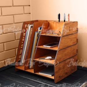 May include: A wooden desktop organiser with multiple compartments for storing office supplies. It features a large section for books or files, a smaller section for pens and pencils, and a shelf for a phone or other small items. The organiser is made of natural wood and has a warm brown finish.