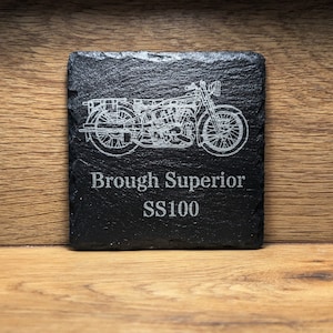 May include: Black slate coaster with a white engraved image of a Brough Superior SS100 motorcycle. The text "Brough Superior SS100" is also engraved on the coaster.