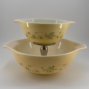 May include: A set of two yellow mixing bowls with a green floral design. The smaller bowl sits on top of the larger bowl with a metal stand.