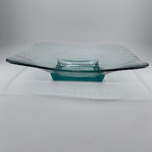May include: A square, clear glass serving bowl with a teal green base. The bowl has a textured, rippled surface.