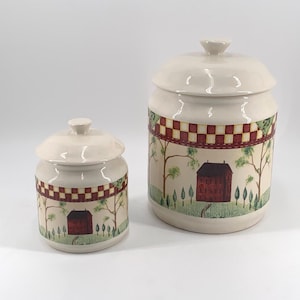 May include: Two ceramic canisters with lids. The canisters are off-white with a decorative band of red and white checkered pattern. The design includes a red barn, trees, and green foliage. The canisters are different sizes.