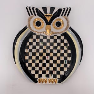 May include: A ceramic owl-shaped decorative plate featuring a black and white checkered pattern on the chest, gold-painted eyes, beak, and talons, with black and white striped ear tufts and a glossy finish throughout the entire surface.