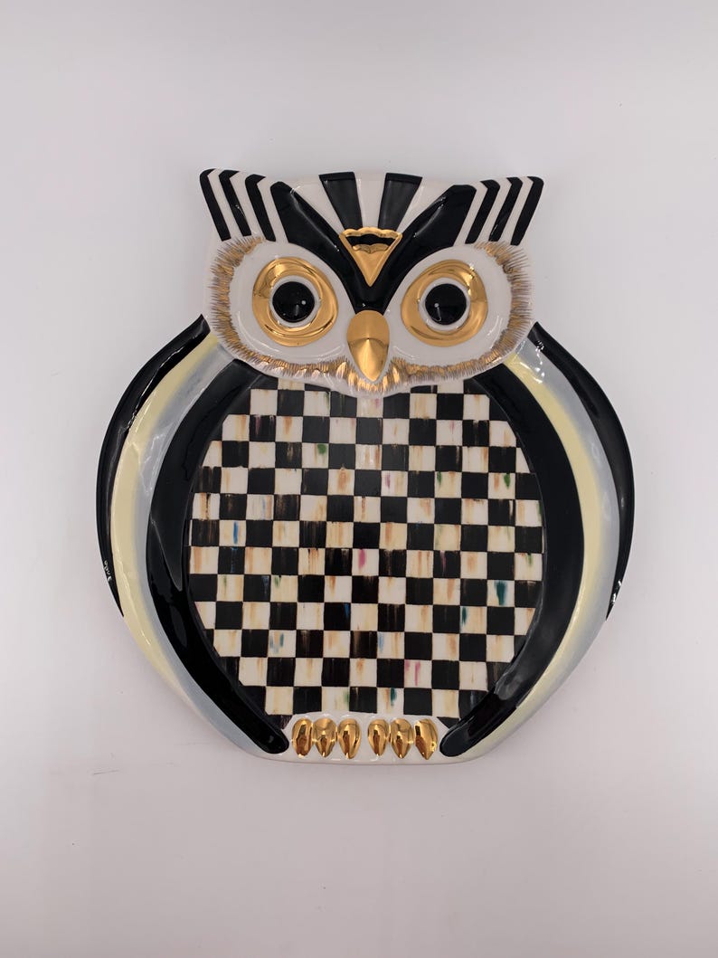 May include: A ceramic owl-shaped decorative plate featuring a black and white checkered pattern on the chest, gold-painted eyes, beak, and talons, with black and white striped ear tufts and a glossy finish throughout the entire surface.