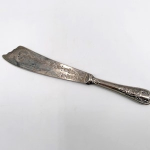 May include: Silver butter knife with ornate floral and leaf design on the blade and handle. The knife has a curved blade and a decorative handle, perfect for spreading butter or other spreads.