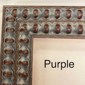 May include: Close-up of a dark gray and red ornate picture frame with a raised bead design. The frame has a light brown mat and the word "Purple" is written in black on the mat.